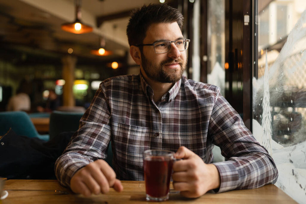 Adult caucasian man sitting alone at cafe front view of one male with beard and eyeglasses holding a cup of tea real people copy space - Zdjęcie, obraz