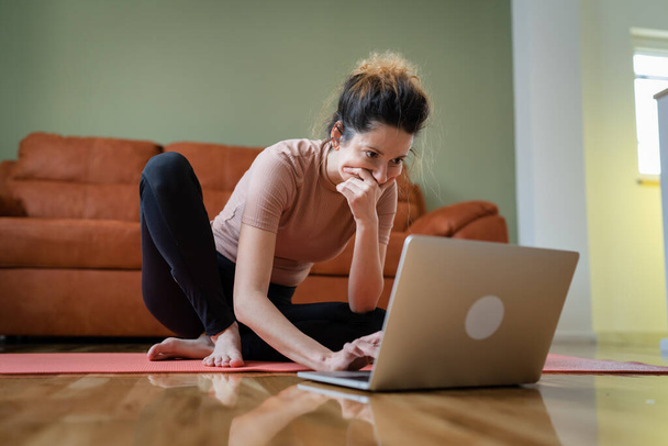 One woman adult caucasian female sitting on the training mat at home using laptop computer to browse internet for online guided training course real people self care concept copy space - Photo, image