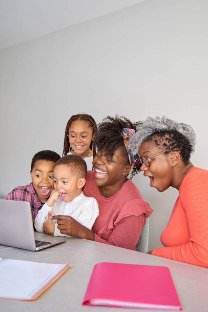 Happy african horizontal extended family look at laptop screen surprised and laughing at home. - Foto, afbeelding