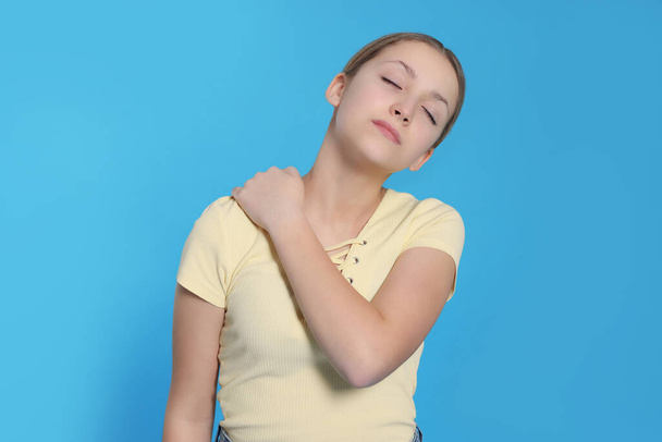 Teenage girl suffering from pain in shoulder on light blue background. Arthritis symptom - Foto, Bild