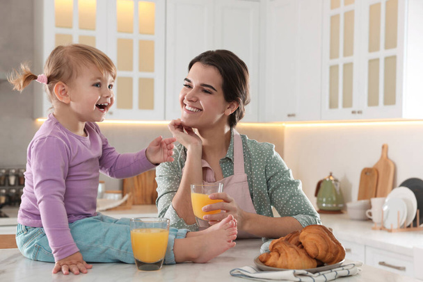 Mother and her little daughter having breakfast together in kitchen - Фото, зображення
