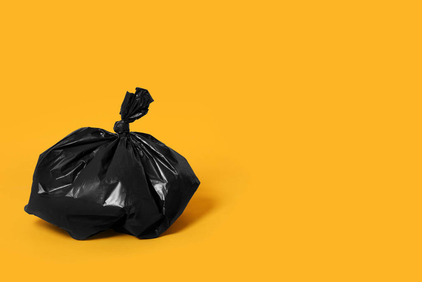 Trash bag full of garbage on orange background. Space for text - Zdjęcie, obraz