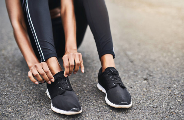 Los zapatos correctos marcan la diferencia. Primer plano de una mujer deportiva atándose los cordones mientras hace ejercicio al aire libre - Foto, imagen
