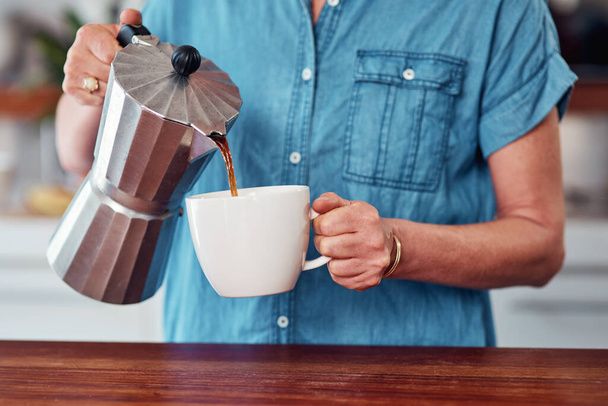 Hän aloittaa aamun kofeiinilla. tunnistamaton vanhempi nainen kaataa itselleen kupin kahvia seistessään keittiössä - Valokuva, kuva