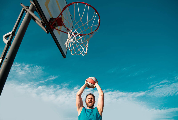 Mature man holding basketball against clear blue sky - Фото, зображення