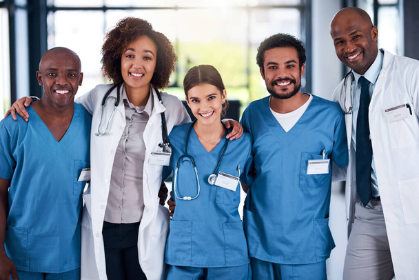 There is no other better team around. Portrait of a cheerful group of doctors standing with their arms around each other inside of a hospital during the day - 写真・画像