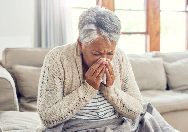 Oudere vrouw, ziek en snuit neus thuis van virus, allergie en ziekte op de bank. Moe, weefsel en bejaarde vrouw in een huiskamer met niezen van covid en griep op een bank met allergieën. - Foto, afbeelding