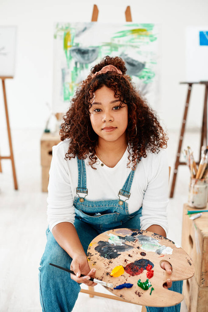 Be confident enough to let creativity run free. Cropped portrait of an attractive young artist sitting alone in the studio and holding a palette during an art class - Photo, Image