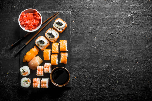 Rotoli di sushi giapponesi tradizionali con zenzero e salsa di soia su una tavola di pietra nera. Su sfondo nero rustico
 - Foto, immagini