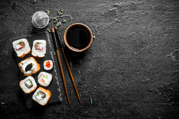 Various Japanese rolls with soy sauce and chopsticks. On black rustic background - Foto, immagini