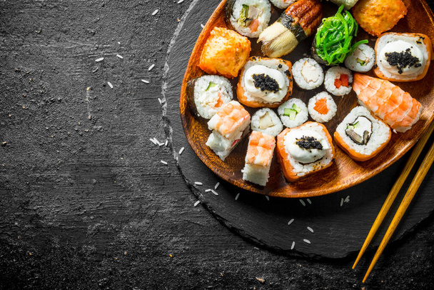Assortment of different sushi rolls on a plate with chopsticks. On black rustic background - Foto, imagen