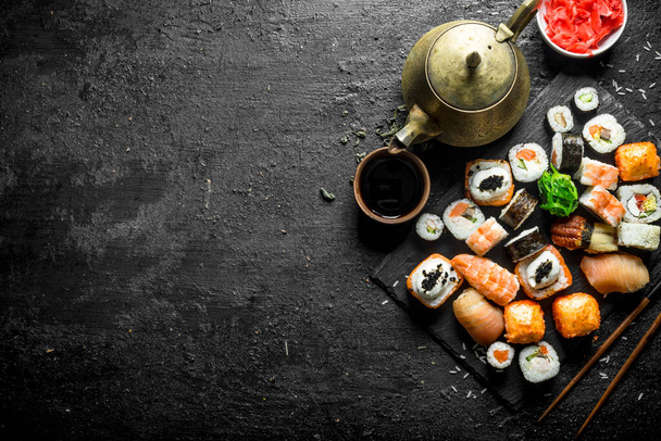 Various kinds of Japanese sushi rolls with ginger and soy sauce. On black rustic background - Foto, Imagen
