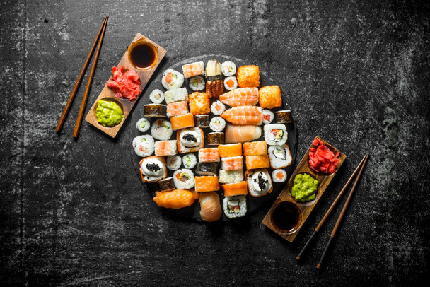 Delicious Japanese rolls with sauce and chopsticks. On dark rustic background - Photo, Image