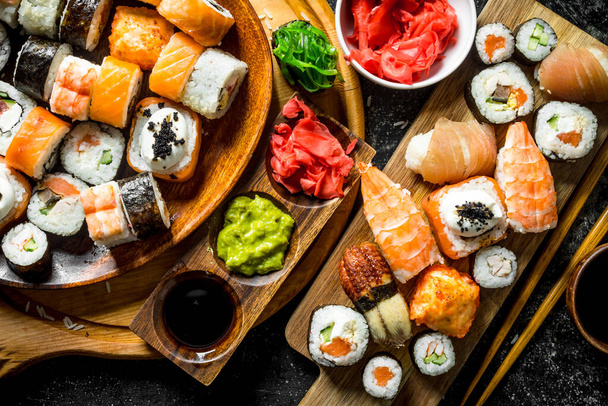 A variety of sushi, maki and rolls with ginger and soy sauce. On rustic background - Фото, изображение