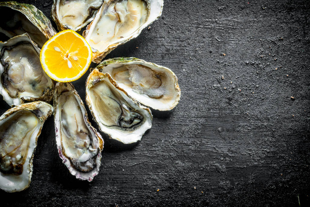 Fresh oysters with lemon. On black rustic background - 写真・画像