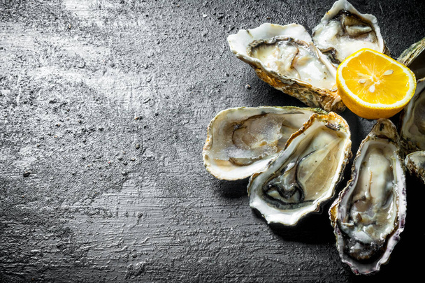 Fresh oysters with lemon. On black rustic background - Valokuva, kuva