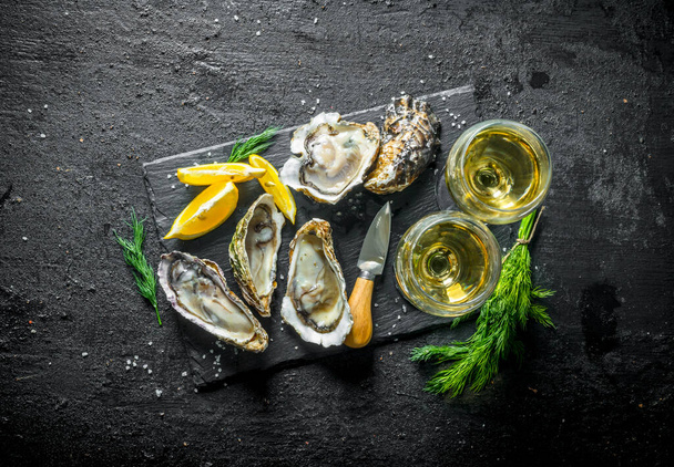 Fresh raw oysters on a stone Board with white wine. On black rustic background - Fotoğraf, Görsel