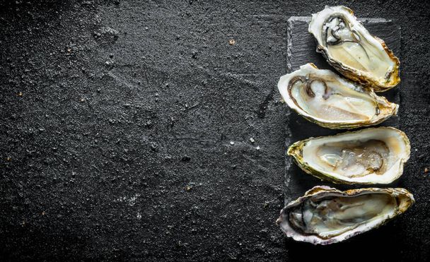 Opened fresh oysters on a stone stand. On black rustic background - Fotoğraf, Görsel