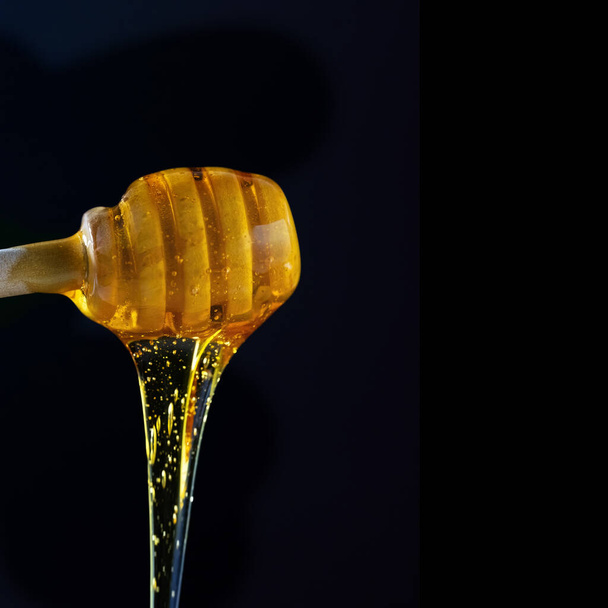 Мед капает с деревянного меда палку на черном фоне - Фото, изображение