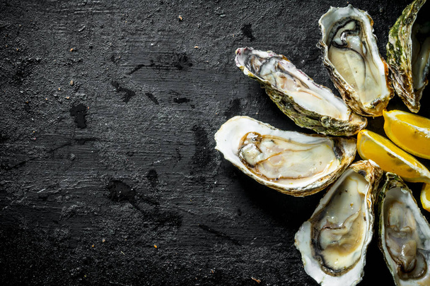 Delicious raw oysters with lemon slices. On black rustic background - Foto, afbeelding
