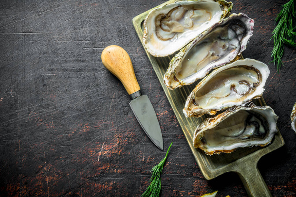 Seafood. Raw Opened oysters on a cutting Board with knife. On dark rustic background - Fotografie, Obrázek