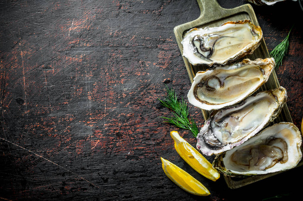 Delicious fresh oysters with lemon slices and dill. On dark rustic background - Foto, afbeelding