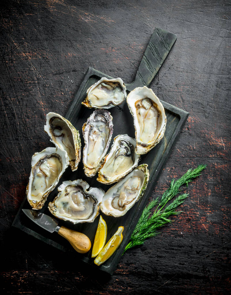 Fresh oysters on a cutting Board with dill and lemon. On dark rustic background - Foto, immagini