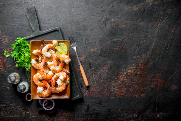 Shrimps on a cutting Board with parsley, spices and lime. On dark rustic background - Zdjęcie, obraz