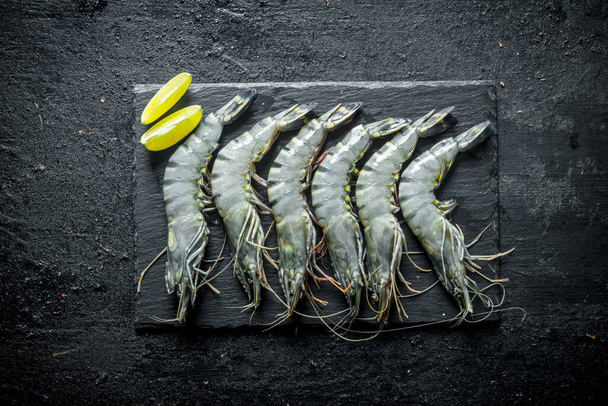 Fresh raw shrimps on a stone Board with lime slices. On black rustic background - Φωτογραφία, εικόνα