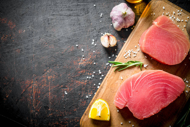 Fresh raw tuna on a cutting Board with lemon and garlic. On dark rustic background - Foto, Bild