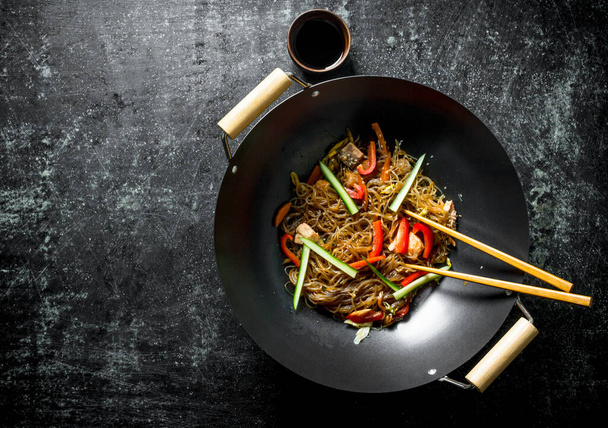 Chinese wok. Aziatische cellofaan noedels met groenten en kip in een koekenpan wok. Op donkere rustieke achtergrond - Foto, afbeelding