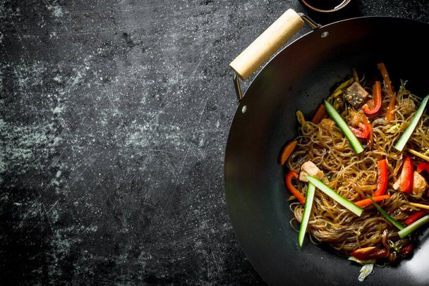 Chinese wok. Asian cellophane noodles with vegetables and chicken in a frying pan wok. On dark rustic background - Foto, afbeelding