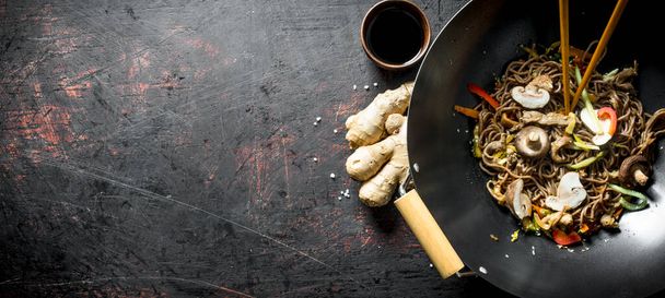 Fragrant soba noodles in a wok pan with mushrooms and fresh vegetables. On dark rustic background - Zdjęcie, obraz