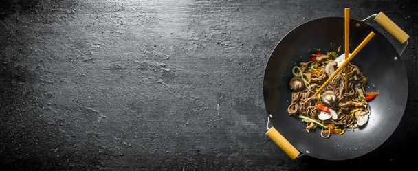 Chiński makaron Wok soba na patelni z pałeczkami. Na czarnym tle rustykalnym - Zdjęcie, obraz