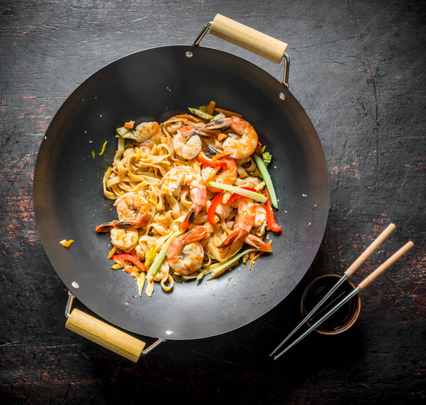 Chinese wok. Udon noodles in a wok pan with chopsticks and soy sauce. On dark rustic background - Photo, image