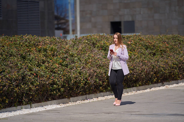 Νεαρή επιχειρηματίας κάνει μια βόλτα μετά τη δουλειά, ενώ συνομιλεί στο κινητό της τηλέφωνο - Φωτογραφία, εικόνα