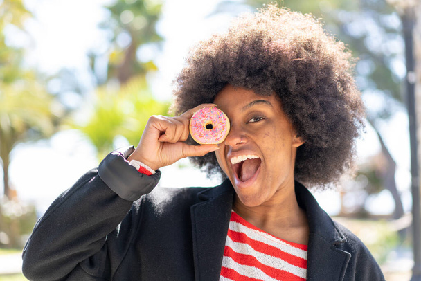 Chica afroamericana al aire libre sosteniendo donuts en un ojo - Foto, Imagen