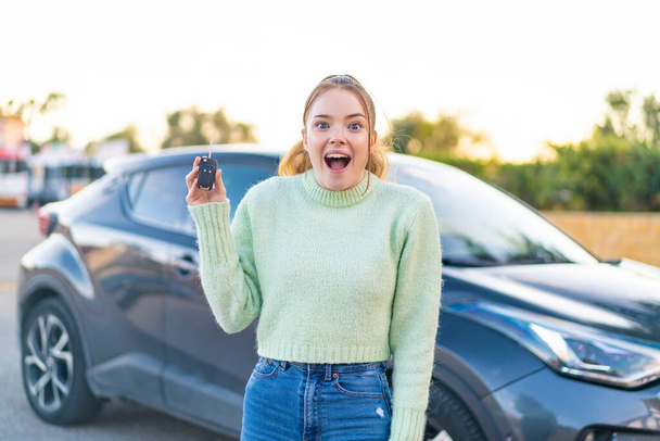 Молода красива дівчина тримає ключі від автомобіля на відкритому повітрі з несподіваним і шокованим виразом обличчя
 - Фото, зображення