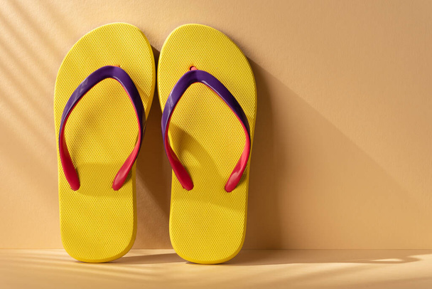 Yellow flip flops with a palm leaves shadow. Summer background concept. - Fotografie, Obrázek
