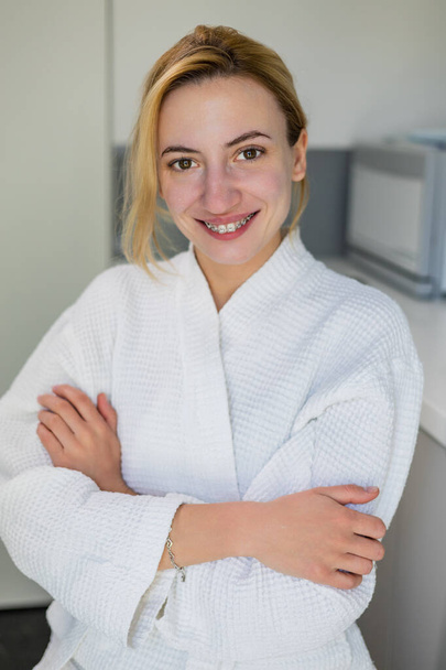 Smiling beautiful girl with natural beauty face with out make up, wearing braces and a white robe, smiles at the camera after beauty procedures, skin rejuvenation, in a beauty clinic, spa salon - Photo, Image
