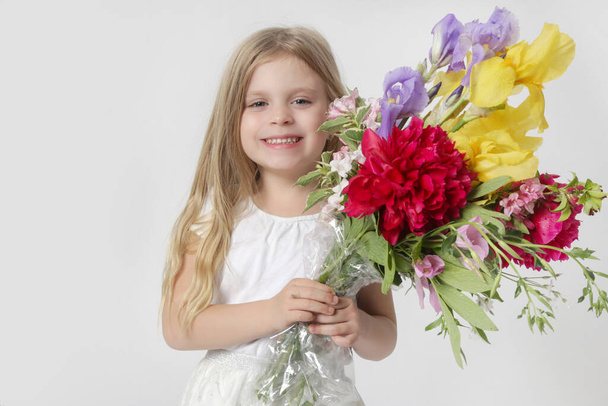 Studio portrait of beautiful little girl holding big colorful bouquet of various flowers. - Photo, Image
