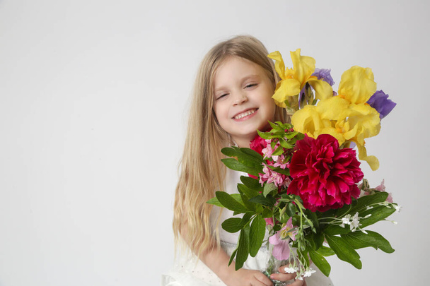 Studio portrait of beautiful little girl holding big colorful bouquet of various flowers. - Photo, Image
