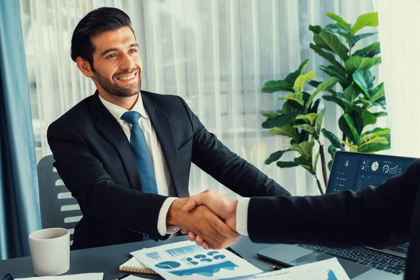 Closeup professional businessman shaking hands over desk in modern office after successfully analyzing pile of dashboard data paper as teamwork and integrity handshake in workplace concept. fervent - Foto, Imagen