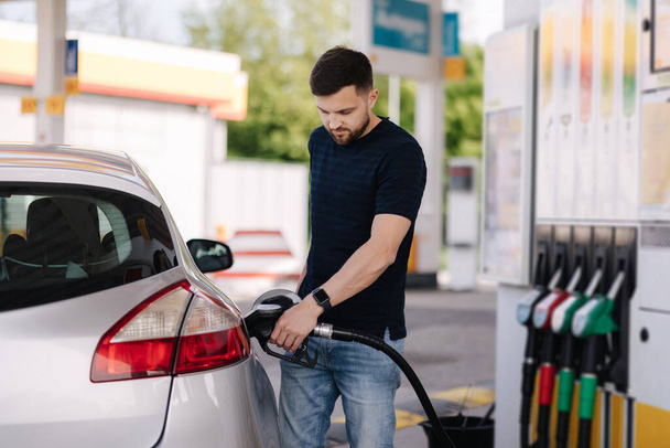 Handsome young man refuelling car at gas station. Female filling diesel at gasoline fuel in car using a fuel nozzle. Petrol concept. Side view. High quality photo - Fotó, kép