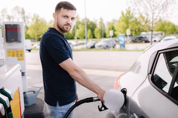 Benzin istasyonunda arabasına yakıt dolduran yakışıklı bir adam. Benzin deposunda yakıt enjektörü kullanan bir erkek. Benzin kavramı. Yüksek kalite fotoğraf - Fotoğraf, Görsel