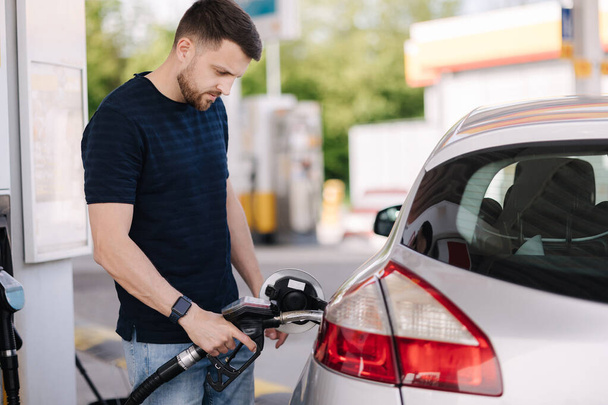 Handsome bearded man refueling car at self service gas station. Petrol concept. High quality photo - Foto, afbeelding
