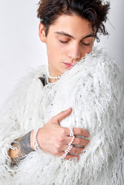 charming cute male model with natural make-up posing hugging himself, isolated on white background. portrait of young gay in modern elegant clothes, in fluffy jacket. feminine, bisexual - Foto, afbeelding