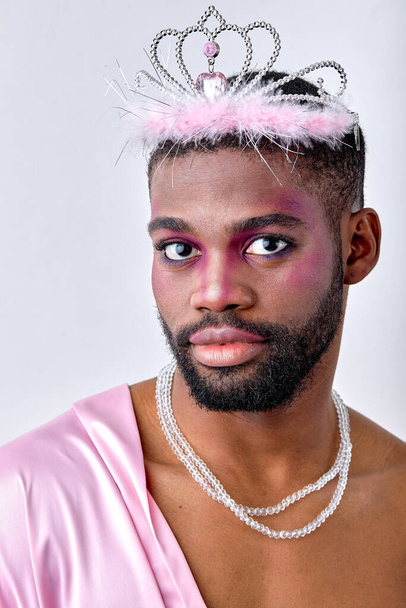 Nice male princess of black american appearance posing, half-naked man in stylish pink silk shirt with make-up alone. bodypositive, lgbtq, homosexual, transgender, beauty, fashion concept - Photo, image