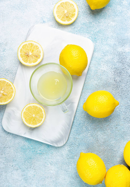 A cup of squeezed lemon juice and lemons, slices of lemons around. Bright background. Summer concept - Photo, Image