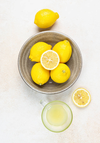Una taza de jugo de limón exprimido y limones, rodajas de limones alrededor. Fondo brillante. Concepto de verano - Foto, imagen